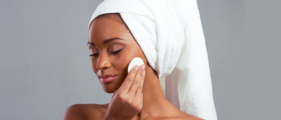 Black woman applying cream for her face while she is wearing towel on her head